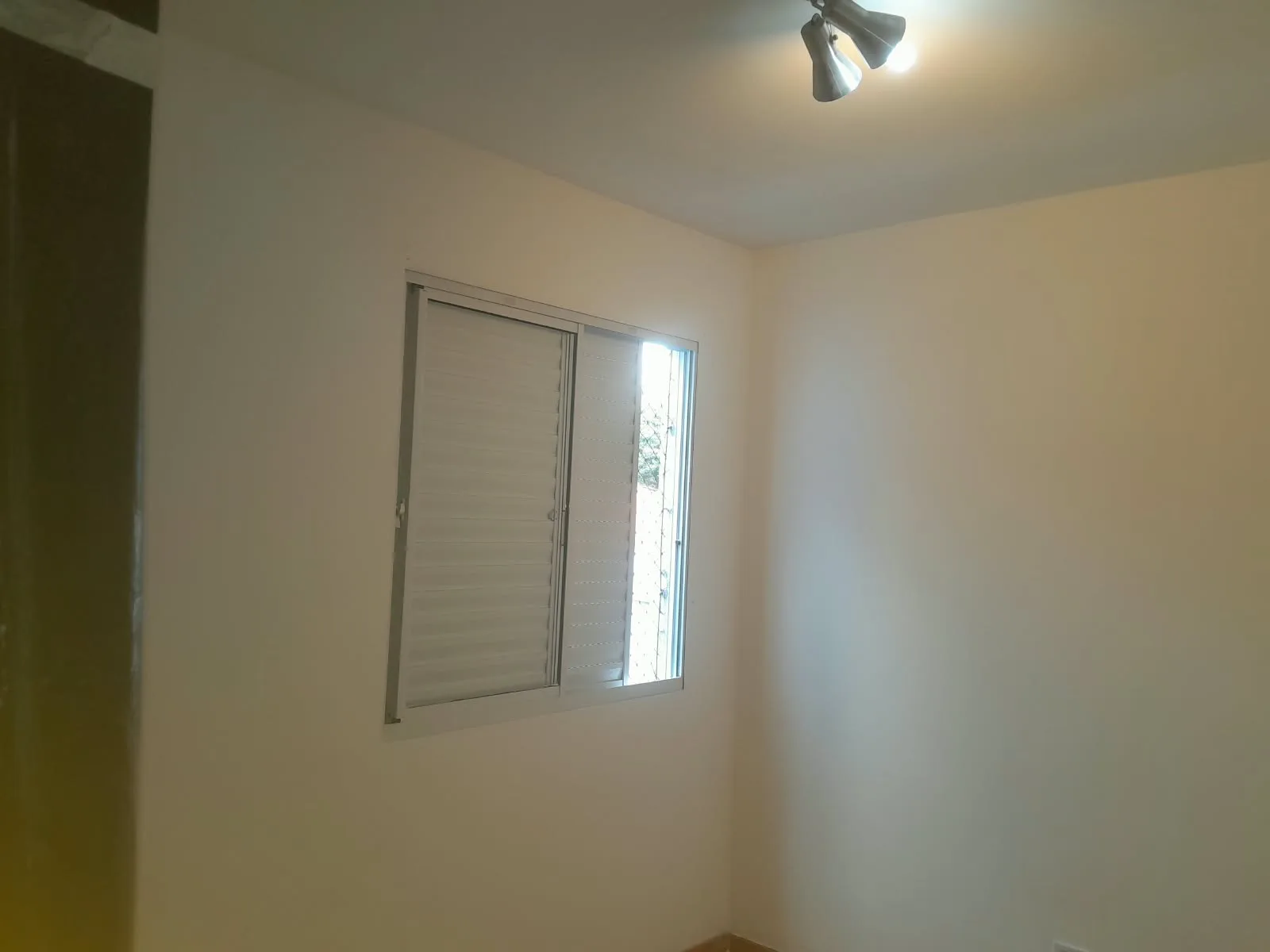 Quarto de paredes brancas lisas, com janela e luminária no teto
